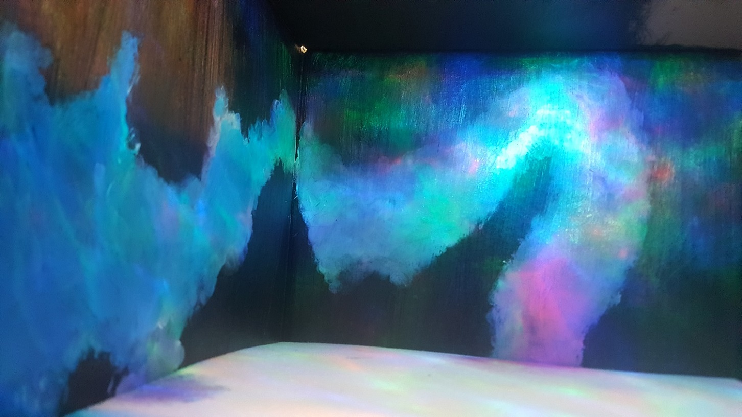 Dark abstract painterly projection of coloured blue and pink light on a black corner wall