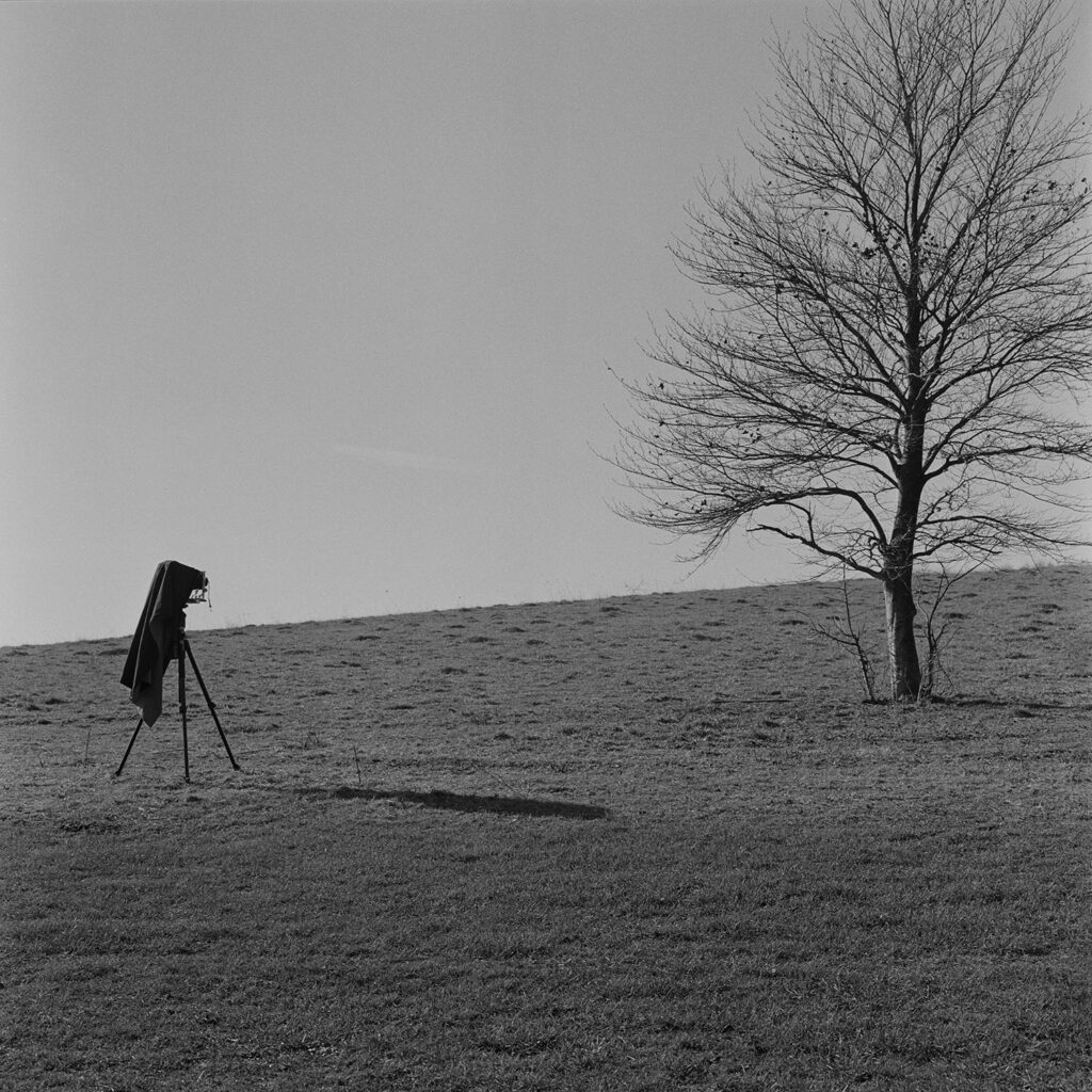 Black and white photograph of old camera and tripod in a field